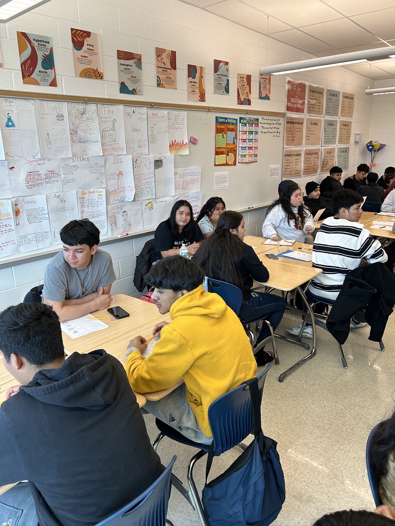 Secondary students collaborating at desks with literacy posters on walls